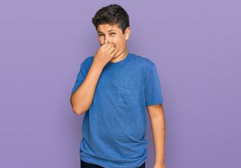 Wall Mural - Teenager hispanic boy wearing casual clothes smelling something stinky and disgusting, intolerable smell, holding breath with fingers on nose. bad smell