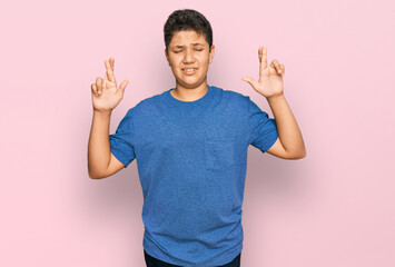 Wall Mural - Teenager hispanic boy wearing casual clothes gesturing finger crossed smiling with hope and eyes closed. luck and superstitious concept.