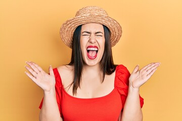 Poster - Young hispanic woman wearing summer hat celebrating mad and crazy for success with arms raised and closed eyes screaming excited. winner concept