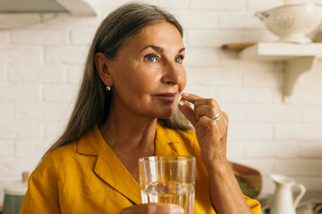 Cute mature female holding drugs and glass of water in hands. Elderly woman taking medication. Treatment course or vitamins complex idea. Healthy lifestyle and healthcare concept