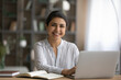 © fizkes - Portrait of happy millennial Indian female student sit at desk study distant on computer. Smiling young mixed race woman work online on modern laptop at home office. Technology, diversity concept.