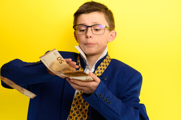 The child scatters money, a boy in a suit throws euros, a portrait of a child on a yellow background.
