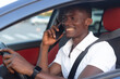 © Alexander - An African-American man sitting behind the wheel of a car with a phone in his hand
