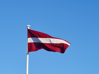 The national flag of Latvia waving in the wind on the flagpole. Horizontal frame.