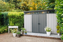 New Garden Shed In Summer. Lots Of Pots Of Flowers Next To A Plastic Garden Shed. Relax In The Garden 