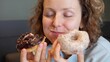 © Sia - Binge eating concept. Attractive Caucasian woman with eating disorder eating two donuts quickly and at the same time