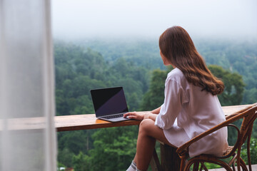 rear view image of a woman using and working on laptop computer while sitting on balcony with a beautiful nature view on foggy day