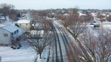 Snowstorm In USA. American Homes In Residential Development. Aerial In Winter Snow. Snowflakes Fall On Street With Tire Tracks. Aerial Establishing Shot.