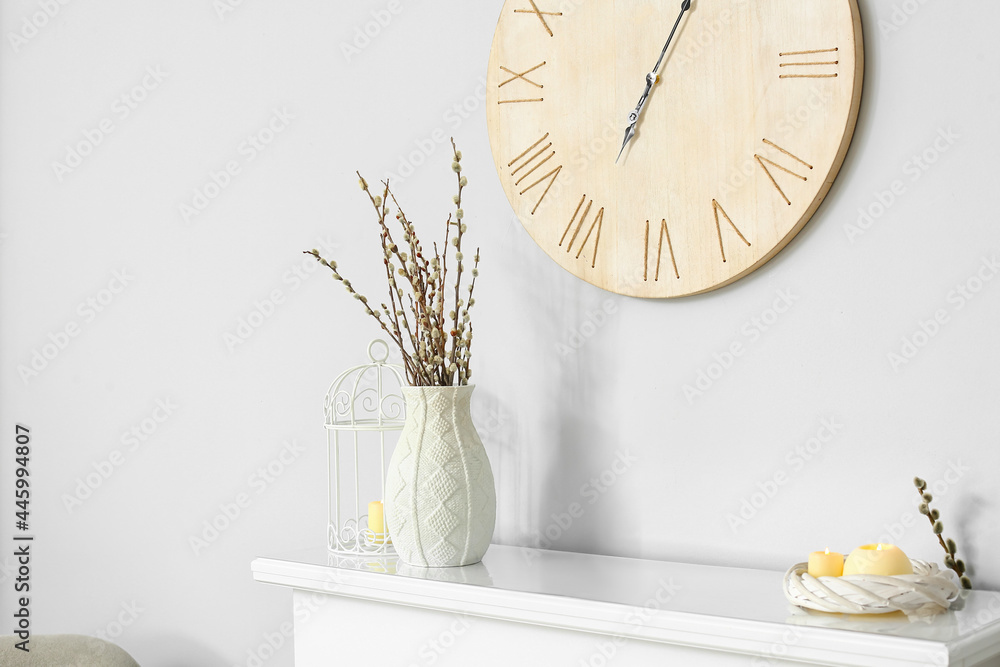 Vase with willow branches and candles on fireplace near white wall - obrazy, fototapety, plakaty 