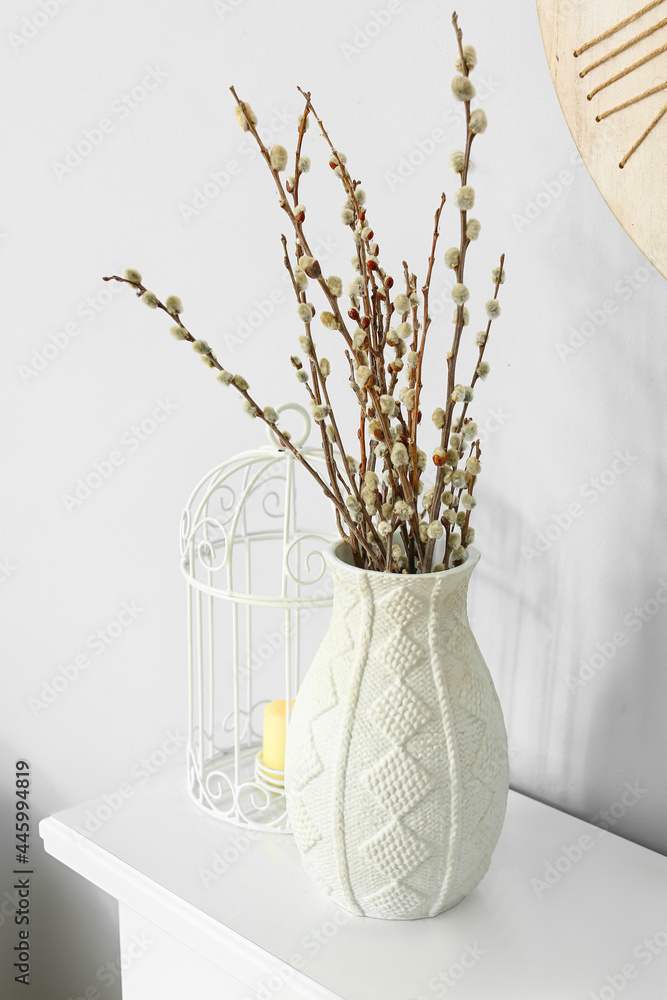 Vase with willow branches on shelf near light wall