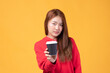 © ueaphan - Portrait of a pretty young Asian woman smile and holding takeaway coffee cup wearing red sweater isolated on yellow background. Beautiful young girl enjoys coffee in the morning.
