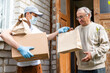 © Angelov - Young delivery man in uniform giving a box, parcel of groceries to elderly man outdoor. Shopping help and delivery service. Volunteer support seniors during coronavirus outbreak