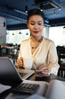 © DragonImages - Business lady in silk blouse working on laptop at restaurant table and checking notifications or answering text messages on her phone