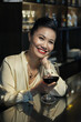 © DragonImages - Portrait of happy elegant woman with glass of red wine sitting at bar counter in restaurant
