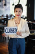 © DragonImages - Sad and tired female restaurant manager showing closed sign and looking at camera
