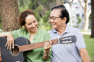 Poster - Proud affectionate senior man looking at his talented wife playing guitar and singing when they are resting in park