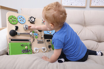 Wall Mural - Cute little boy playing with busy board on sofa at home