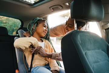 Wall Mural - Black woman smiling while putting her daughter in child seat at car