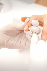 Close up of manicure master with manicure scissors removes cuticles of female nails at beauty salon