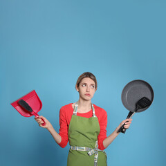 Sticker - Young housewife with dustpan, brush, frying pan and spatula on light blue background