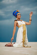 Woman in image of egyptian queen Nefertiti kneels in desert with closed eyes.