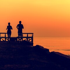 Wall Mural - Healthy young couple running by the beach together in a sunset