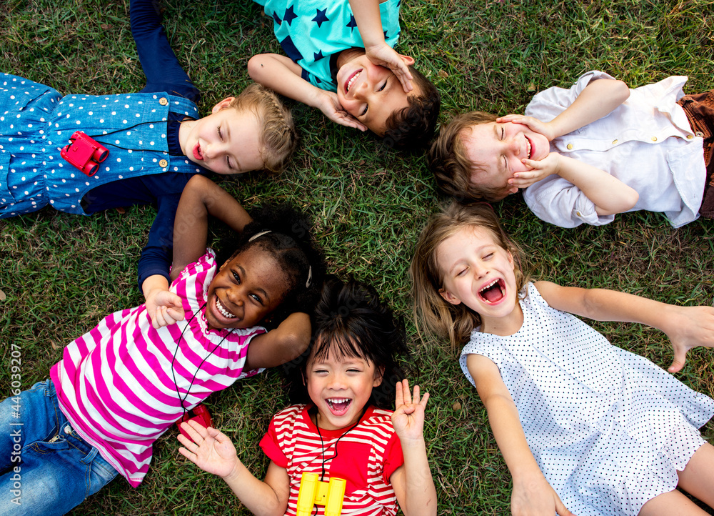 Group of kindergarten kids lying on the grass at park and relax with smiling - obrazy, fototapety, plakaty 