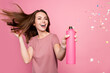 Photo of pretty excited young lady wear casual outfit smiling applying glitter hair spray isolated pink color background