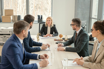 Canvas Print - Group of business people sitting at the table and listening to their leader in the centre during business meeting at office