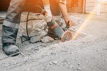 A Worker With A Grinder Cuts The Concrete Pavement Of The Road And Sparks Fly. Construction And Repair Of The Roadway.