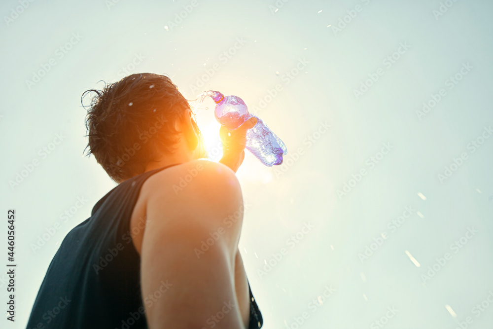 Man pouring water from plastic bottle on his head in hot day - obrazy, fototapety, plakaty 