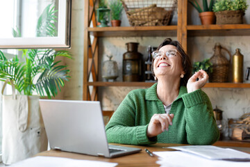 Happy laughing senior woman in front of laptop monitor. She sitting in home interior and having online conversation with relatives or friends.