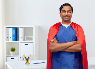 Wall Mural - healthcare, profession and medicine concept - happy smiling indian doctor or male nurse in blue uniform and red superhero cape over medical office at hospital background