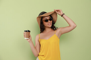 Poster - Beautiful young woman with straw hat and cup of coffee on light green background