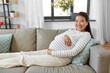© Syda Productions - pregnancy, rest, people and expectation concept - happy smiling pregnant asian woman sitting on sofa at home
