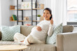 © Syda Productions - pregnancy, rest, people and expectation concept - happy smiling pregnant asian woman sitting on sofa at home and showing thumbs up