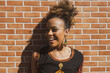 © EZ PHOTOS - Beautiful African American woman leaning against orange bricks wall posing looking away and smiling. Copy space for text.