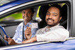 driver courses, exam and people concept - happy smiling indian young man with license and driving school instructor with clipboard in car