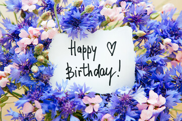 Happy birthday card with greeting words and bouquet of blue cornflower and pink flowers