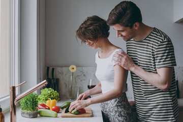 Young side view fun happy couple two smiling caucasian woman man 20s in casual t-shirt clothes prepare vegetable salad cooking food in light kitchen at home together. Healthy diet lifestyle concept.