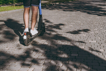 Wall Mural - Cropped up photo shot caucasian young man wearing shorts riding scooter go down city park alley rest relax outdoors on nature openair Urban contemporary transport leisure active lifestyle concept