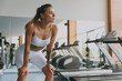 Young tired strong skinny sporty athletic sportswoman woman in white sportswear warm up training near treadmill stand lean on knees look aside breathing in gym indoor Workout sport motivation concept.