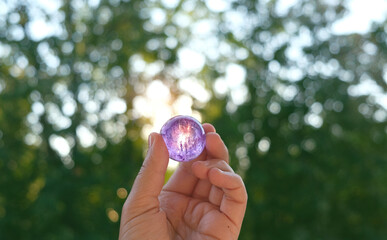 Amethyst quartz crystal ball in hand, natural green background. Esoteric spiritual practice. Mysticism, divination, modern wicca occultism concept. Chakra Relaxation, Wiccan Witchcraft ritual