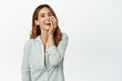 © Cookie Studio - Carefree happy woman in blouse, laughing and smiling cheerful, touching face and looking upbeat at camera, standing against white background
