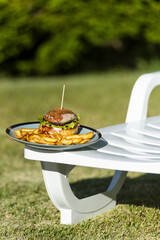 Poster - Vertical shot of a hamburger and potato fry on a plate isolated on a plastic lounge chair