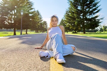 Wall Mural - Fashionable trendy teenage hipster female sitting on road in park