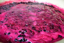 Abstract Background. A Bubbling Surface Of Boiling Jam Made Of Dark Round Berries. Selective Focus, Partially Blurred Jam Texture With Bubbles And Foam