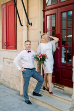 25th Wedding Anniversary. Happy Mature Loving Couple, Handsome Man With His Charming Wife In White Dress, Outdoors In The City, Standing Near Beautiful Vintage Red Door