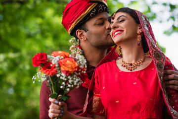 Wall Mural - indian man in turban kissing happy bride in red sari