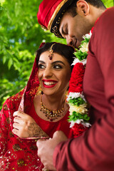 Canvas Print - pleased indian man in turban hugging happy bride in red sari